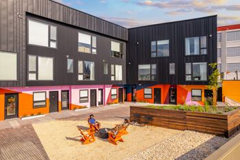 A person is sitting on a chair in a courtyard with a wooden deck and a gravel area.